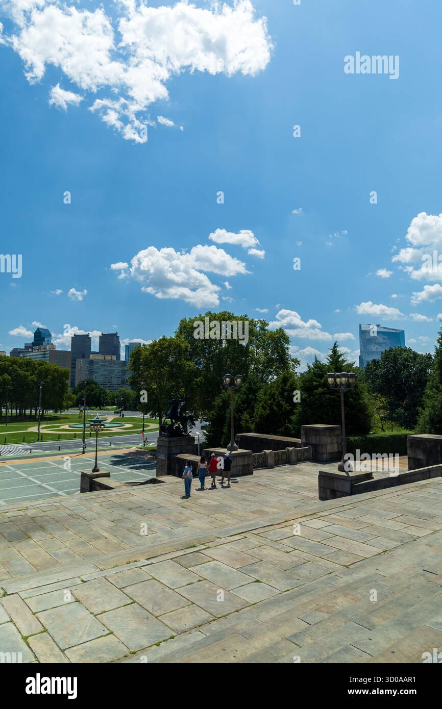 Un gruppo di persone sta camminando lungo una scala di pietra di fronte a una città. Il cielo è blu con alcune nuvole, e la città è sullo sfondo. Philadel Foto Stock Un gruppo di persone sta camminando lungo una scala di pietra di fronte a una città. Il cielo è blu con alcune nuvole, e la città è sullo sfondo. Philadel Foto Stock