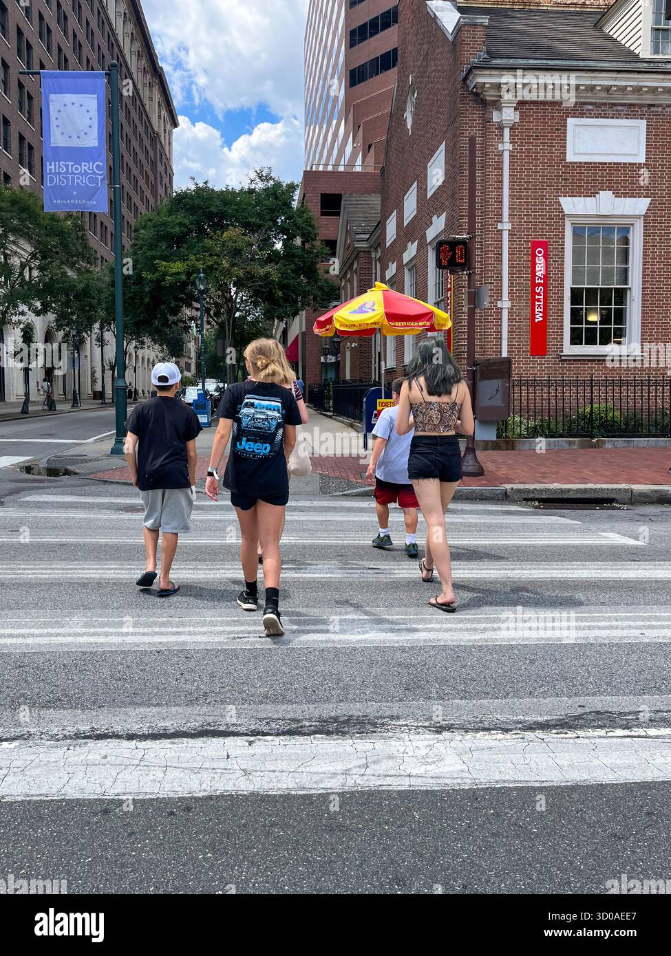 Un gruppo di persone sta attraversando una strada. Una delle persone ha in mano un ombrello rosso Foto Stock Un gruppo di persone sta attraversando una strada. Una delle persone ha in mano un ombrello rosso Foto Stock