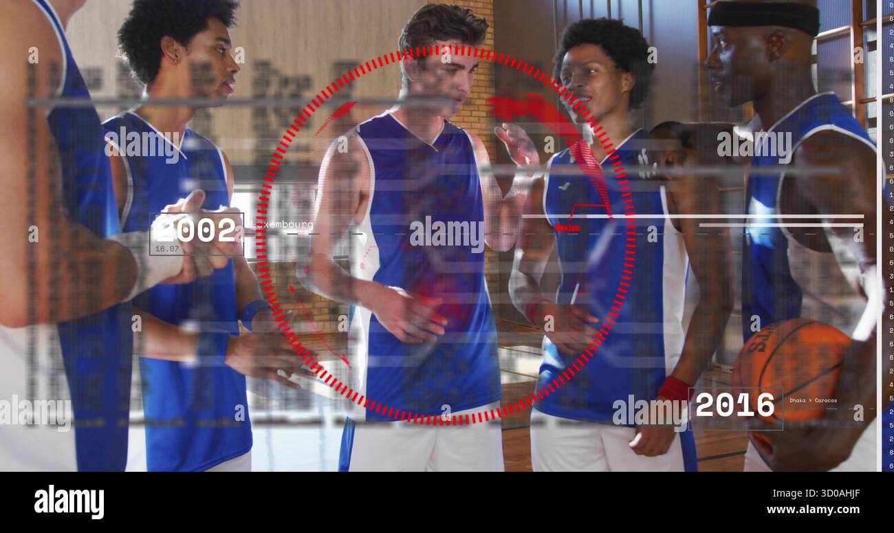 Cinque atleti in maglie abbinate discutono della strategia in palestra, con basket, tablet, rivestimento rosso Foto Stock