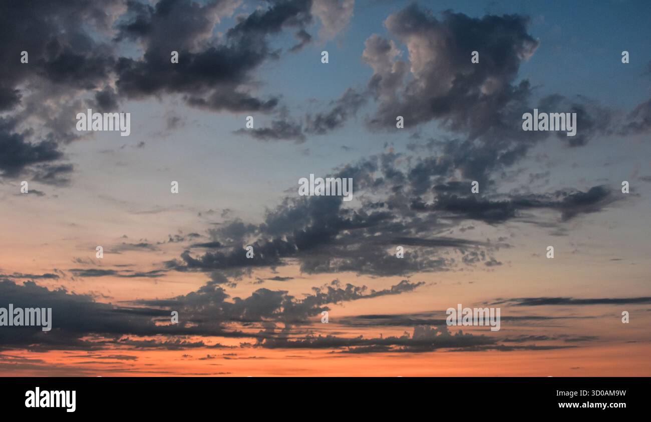 I caldi colori pastello del tramonto illuminano delicatamente il cielo, creando un orizzonte sereno con nuvole scintillanti e magica luce serale. Foto Stock