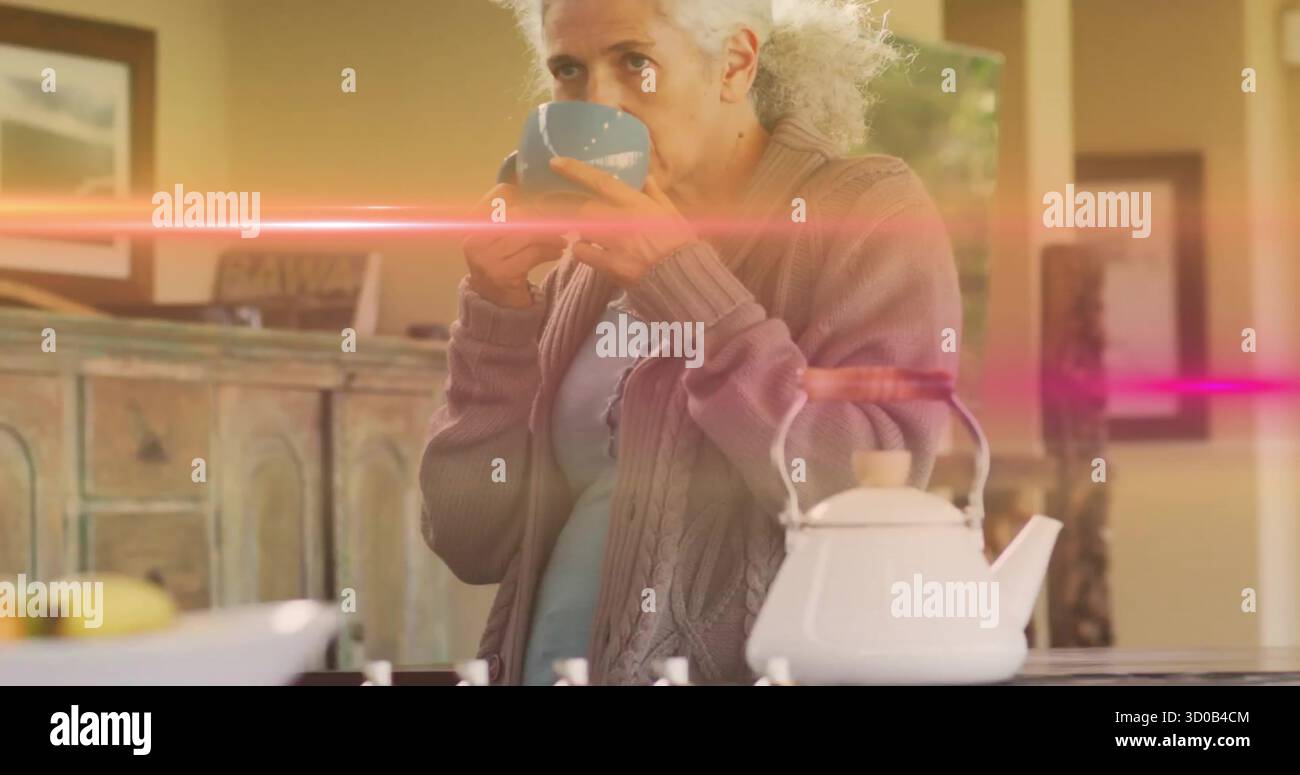 Sorseggia una donna anziana in una tazza di sollevamento del cardigan al bancone della cucina di casa, teiera, cesto di frutta, spazio per le copie Foto Stock