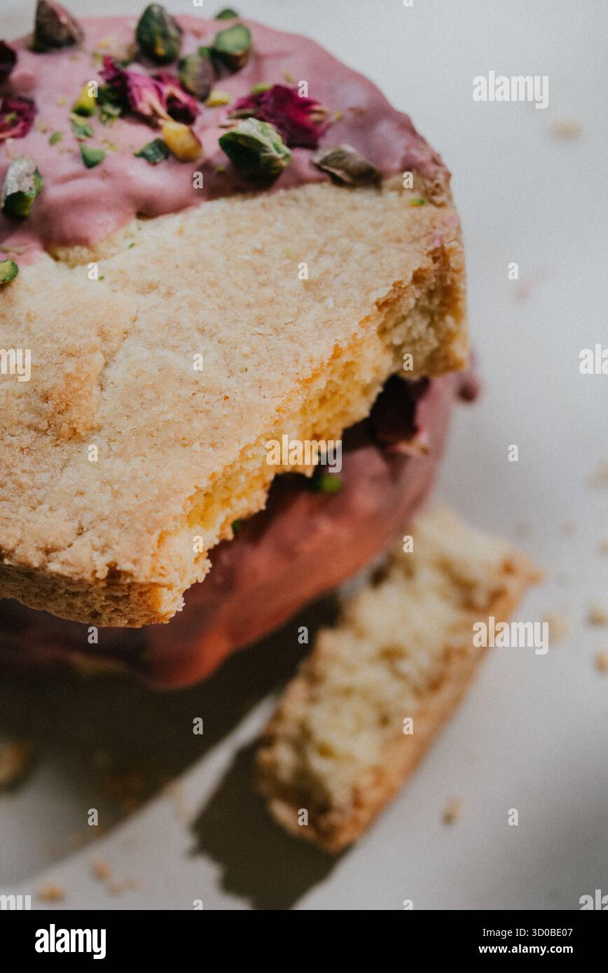 Una fetta di torta con una glassa rosa e un condimento verde. La torta viene tagliata a metà e manca la metà superiore Foto Stock