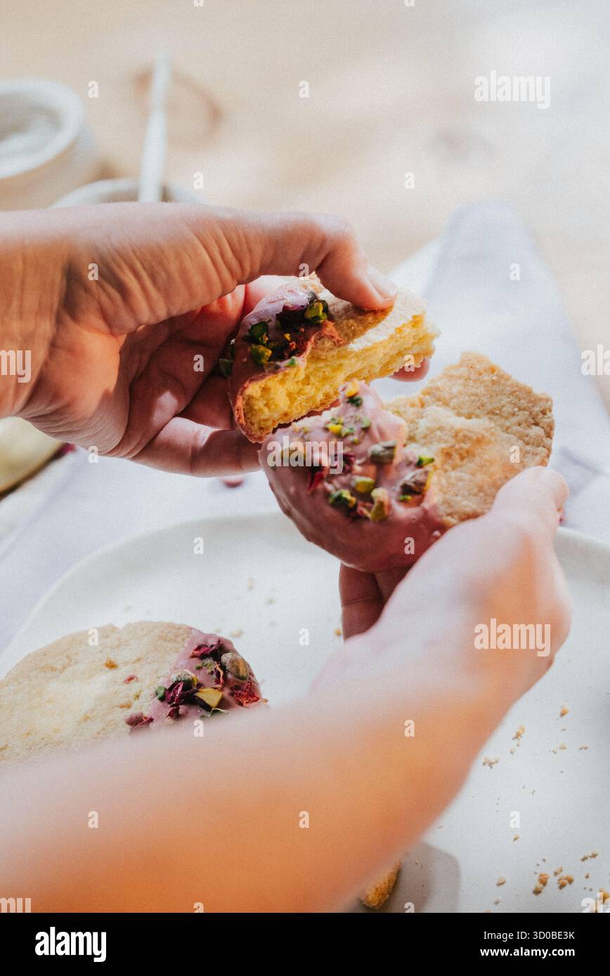 Una persona sta tenendo in mano un pezzo di pasta con una glassa rosa e un condimento verde. La pasticceria è tagliata a metà e la persona sta per prendere un morso. Con Foto Stock