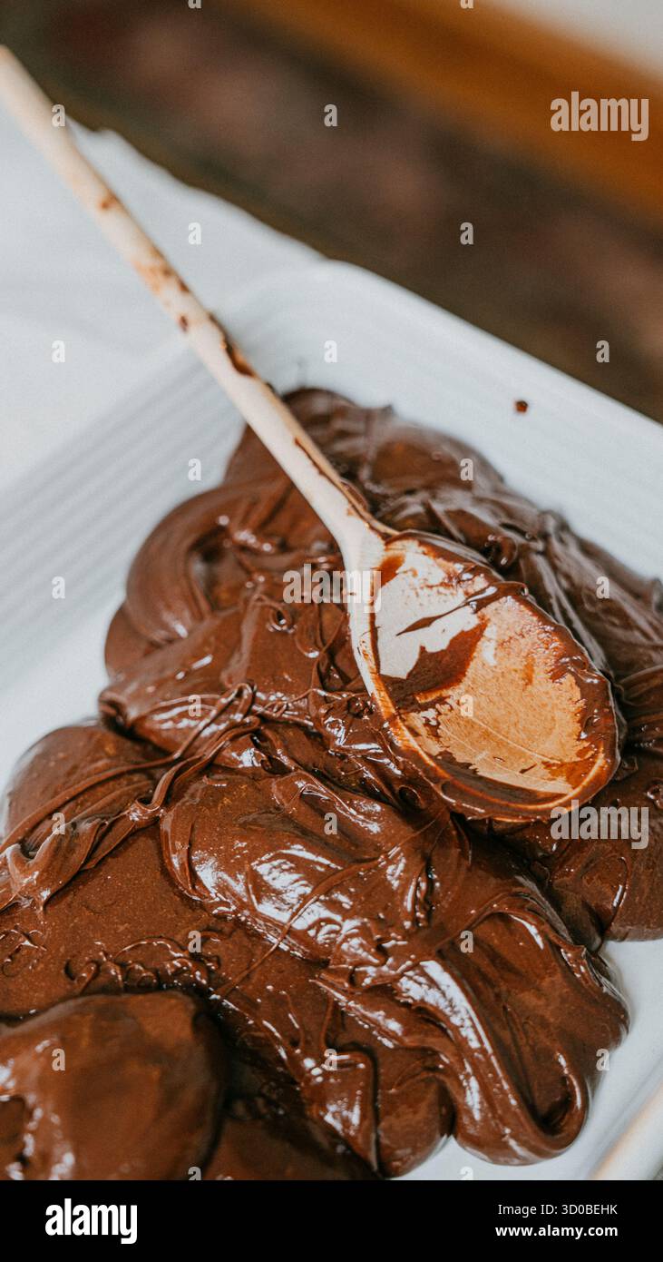 Un cucchiaio di legno viene utilizzato per raccogliere un composto di cioccolato denso e gustoso. Il cucchiaio è ricoperto di cioccolato e il composto viene distribuito su un piatto bianco Foto Stock
