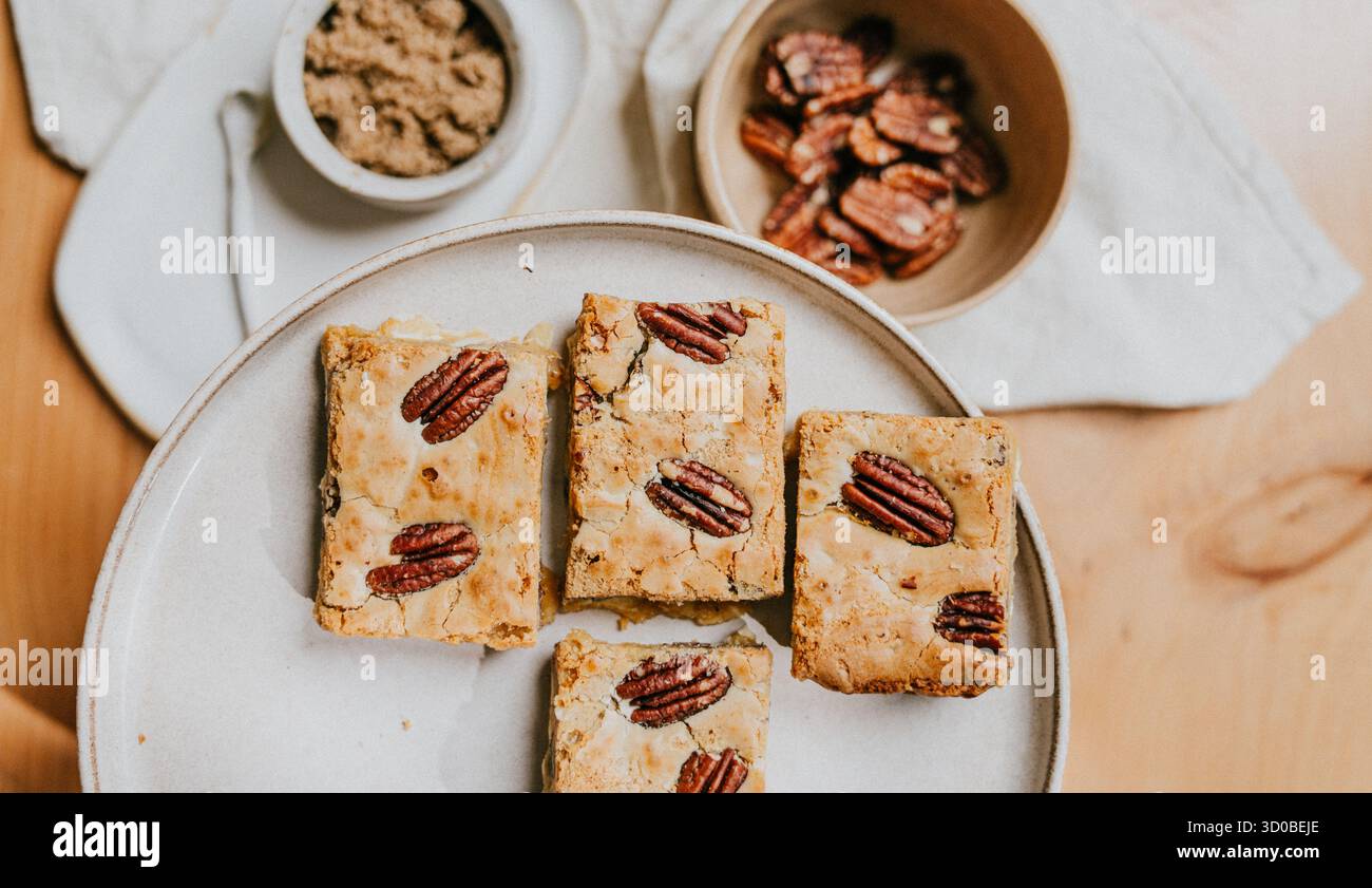 Un piatto di quattro pezzi di dessert con una ciotola di noci sullo sfondo. Il dessert è un tipo di torta con un condimento di noci Foto Stock