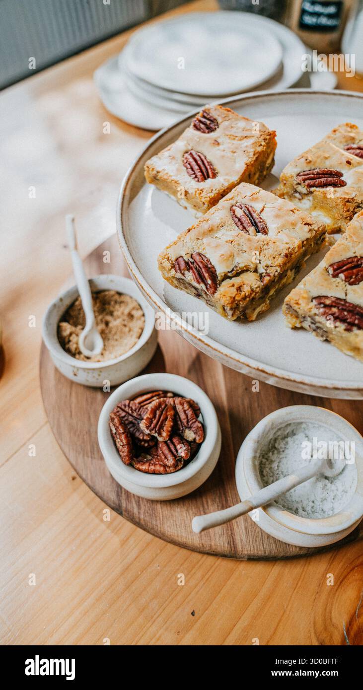 Un piatto di brownie con un vassoio di legno sotto. Sul vassoio sono presenti tre ciotole, una delle quali contiene un cucchiaio Foto Stock