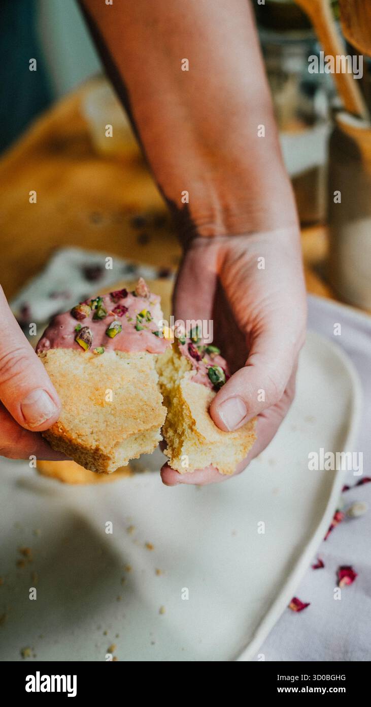 Una persona sta tenendo in mano un dolce con una glassa rosa e una copertura verde. La pasticceria è mezza mangiata e la persona la sta tenendo in mano per mostrarla Foto Stock