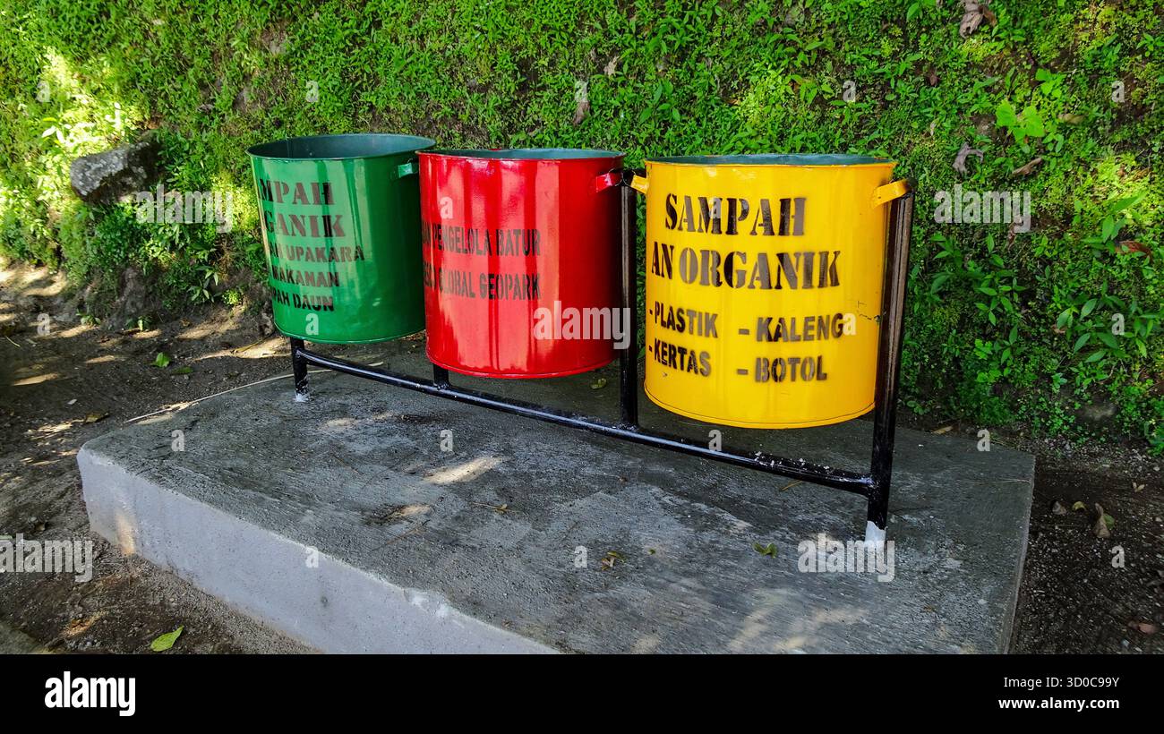 Grandi pentole da cucina verdi, rosse e gialle posizionate sul ciglio della strada a Bali, utilizzate per la separazione dei rifiuti con contrassegni etichettati per il riciclaggio e la rimozione dei rifiuti Foto Stock