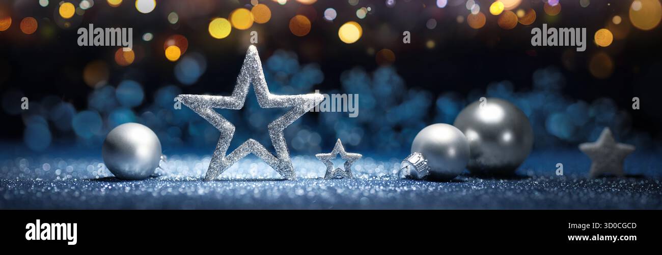 Ornamenti natalizi in argento su una superficie blu scintillante, con luci natalizie su sfondo scuro Foto Stock