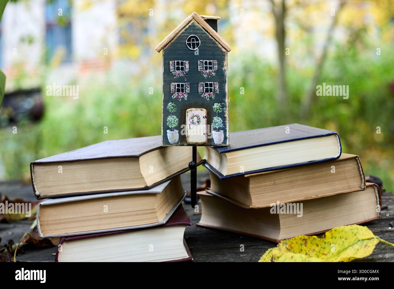 Affascinante casa in miniatura incastonata su una pila di libri in un ambiente autunnale, che crea una scena accogliente e stravagante Foto Stock