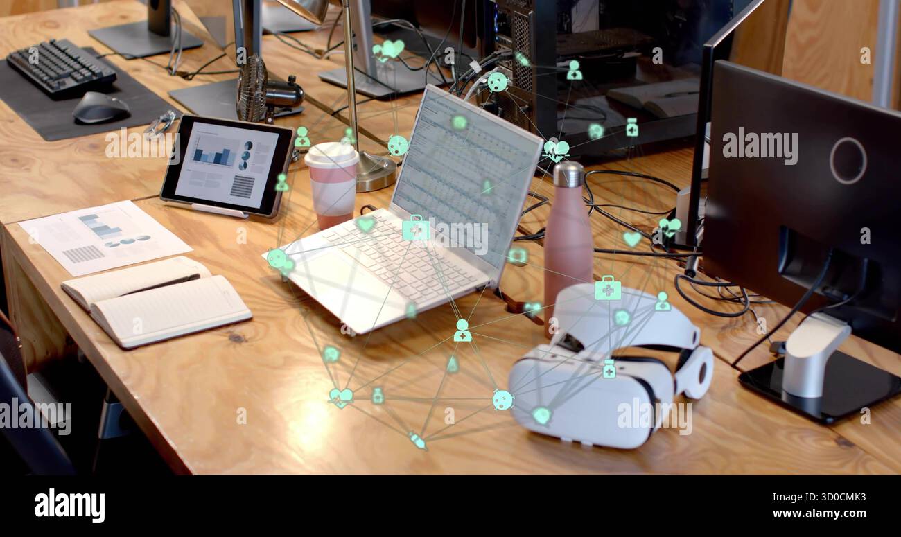 Visualizzazione di un computer portatile color argento con icone di rete sovrapposte sulla scrivania dell'ufficio, con un tablet e una tazza di caffè Foto Stock
