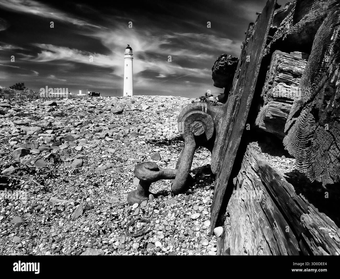 Il Faro di Barns Ness si affaccia sulla costa rocciosa accanto al metallo arrugginito e al legno inalterato in bianco e nero Foto Stock