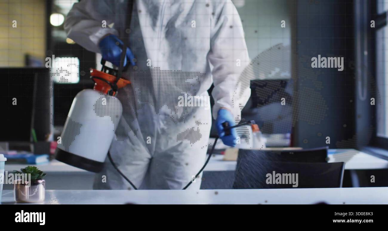 Disinfettante che spruzza alla scrivania dell'ufficio indossando tuta e guanti in nitrile, con spruzzatore Foto Stock