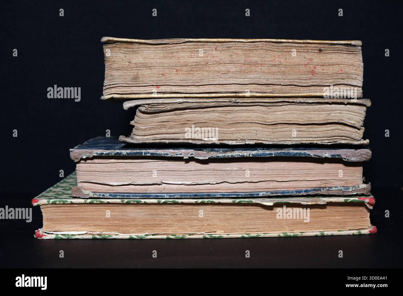 Pile di quattro libri antichi pesanti rilegati in pelle su sfondo nero, che mostrano la consistenza di pagine usurate, vecchie, spine e copertine stracciate. Foto Stock