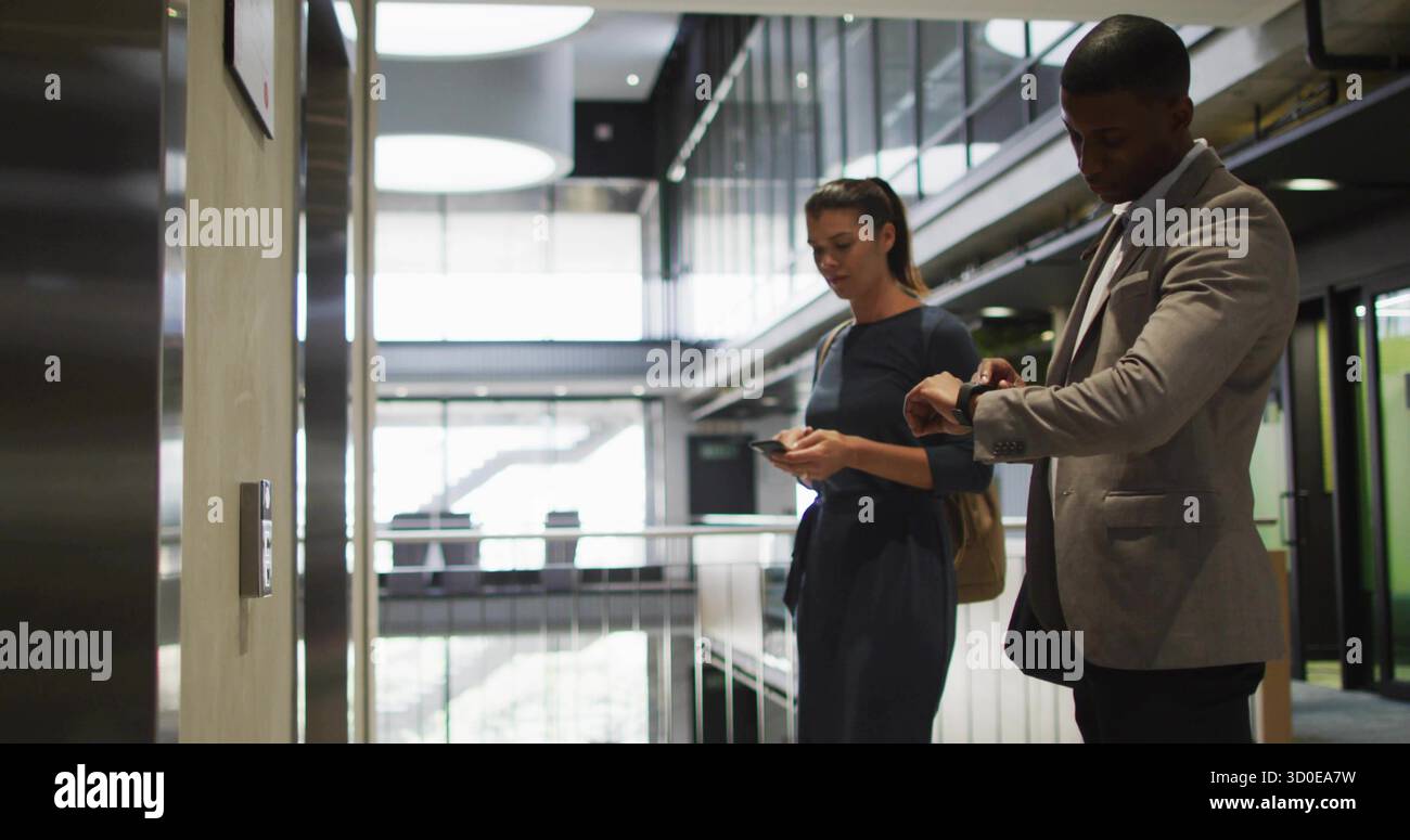 Controllare l'orologio da polso e guardare lo smartphone, abbinare l'abito e vestire al pannello di chiamata dell'ascensore dell'ufficio Foto Stock