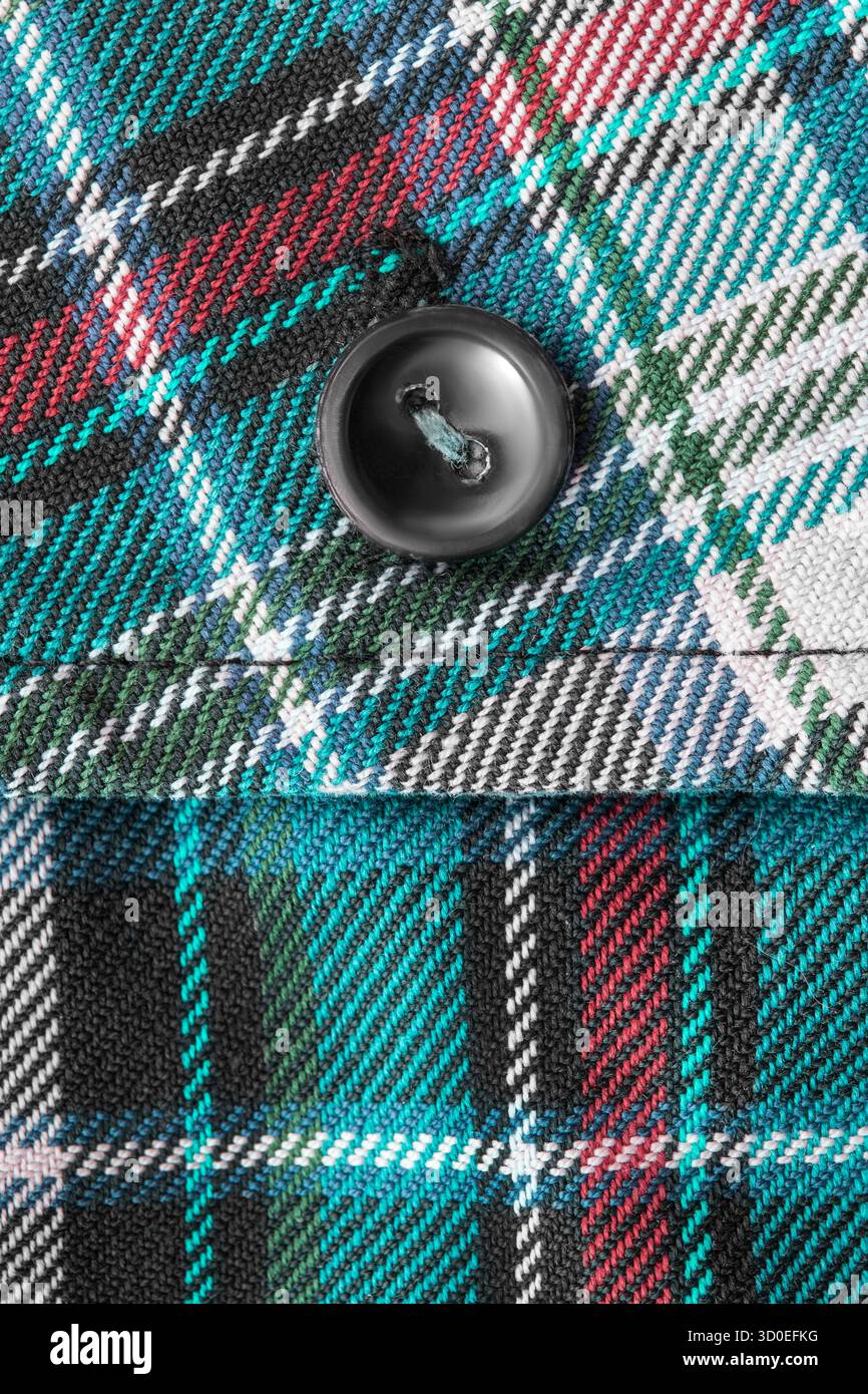 Camicia nera con bottone cucito su sfondo in tessuto tartan colorato Foto Stock