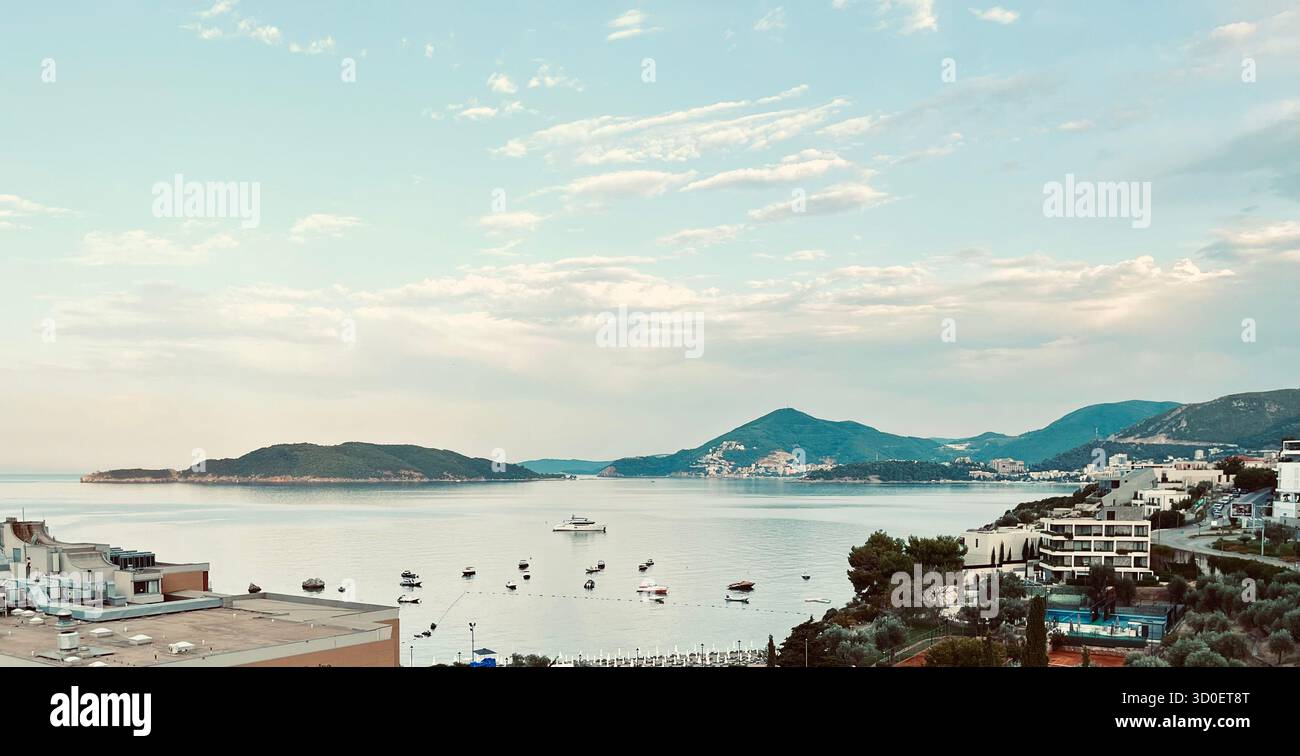 Vista costiera dai toni caldi del mare Adriatico con barche, case sul lungomare e montagne sotto un morbido cielo notturno dorato. - Immagine stock catturata con smartphone
