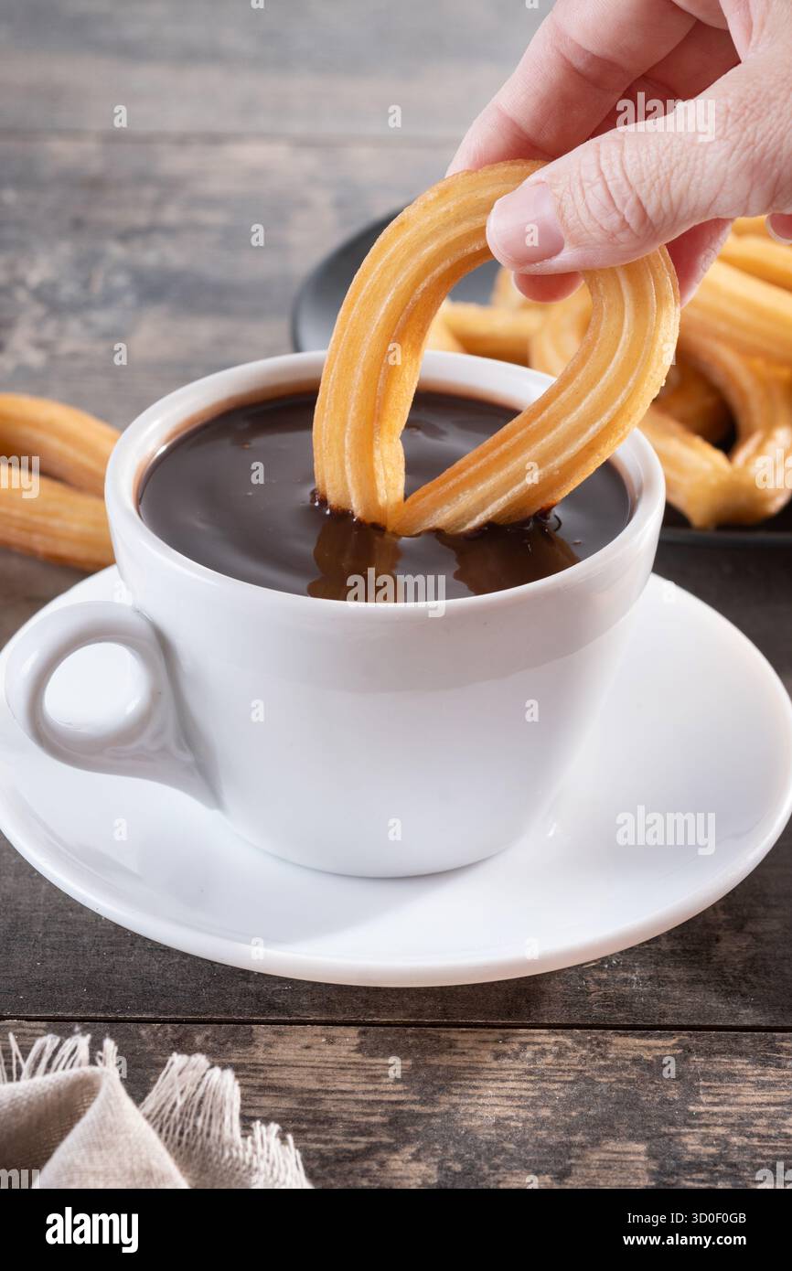 perditi una mano immergendo un churro in una tazza di cioccolata calda. Colazione spagnola tradizionale, Foto Stock