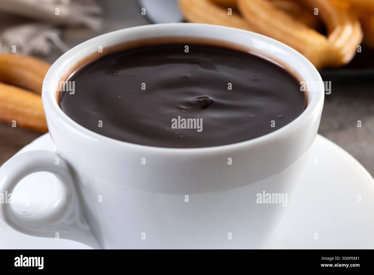 Cioccolata calda spessa in una tazza bianca con churros su un tavolo di legno Foto Stock