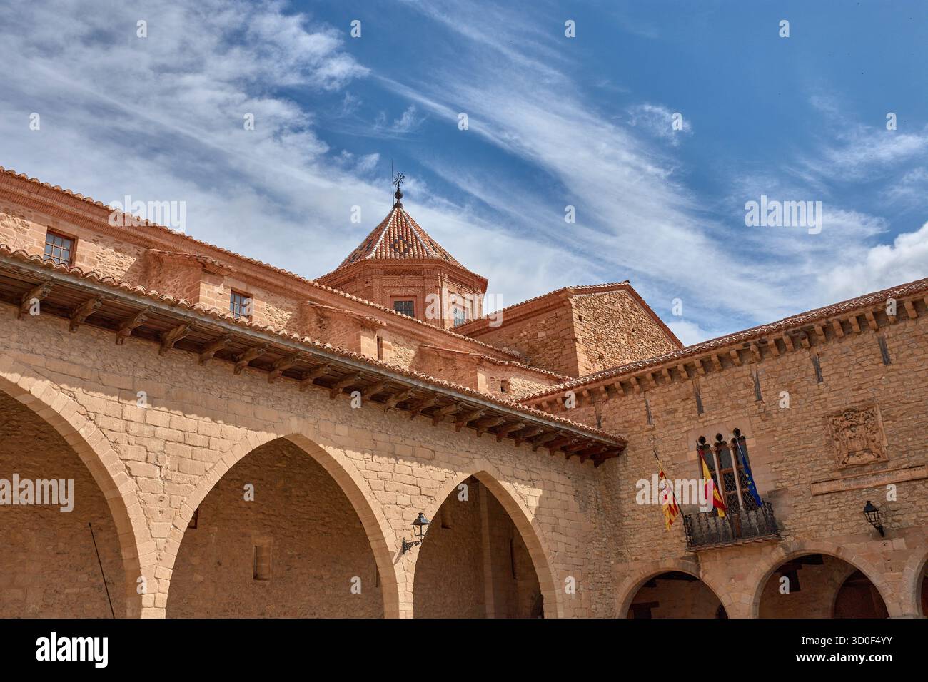 Piazza Cristo Rey a Cantavieja è caratterizzata dalla sua architettura medievale in pietra con archi e balconi adornati con bandiere. I toni caldi del TH Foto Stock