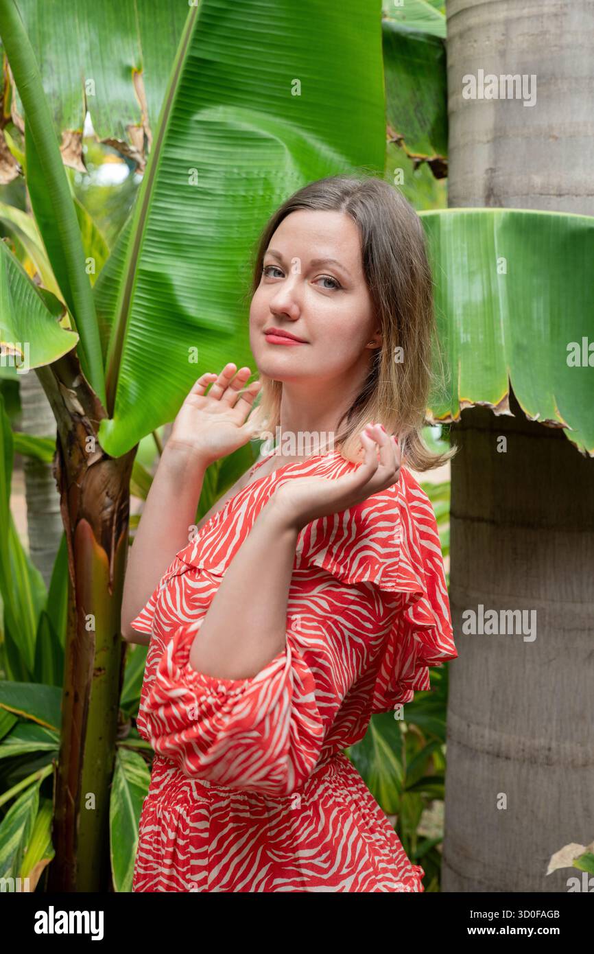 Donna adorabile posizionata leggermente fuori centro, guardando direttamente alla fotocamera con un'espressione morbida e calma e un sorriso sottile mentre si solleva la spalla Foto Stock