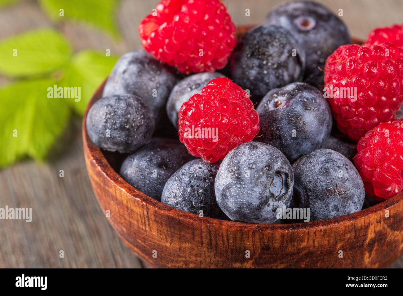 Una foto macro accattivante con lamponi e mirtilli freschi disposti ad arte in una ciotola rustica in legno. I colori vivaci e la texture Foto Stock