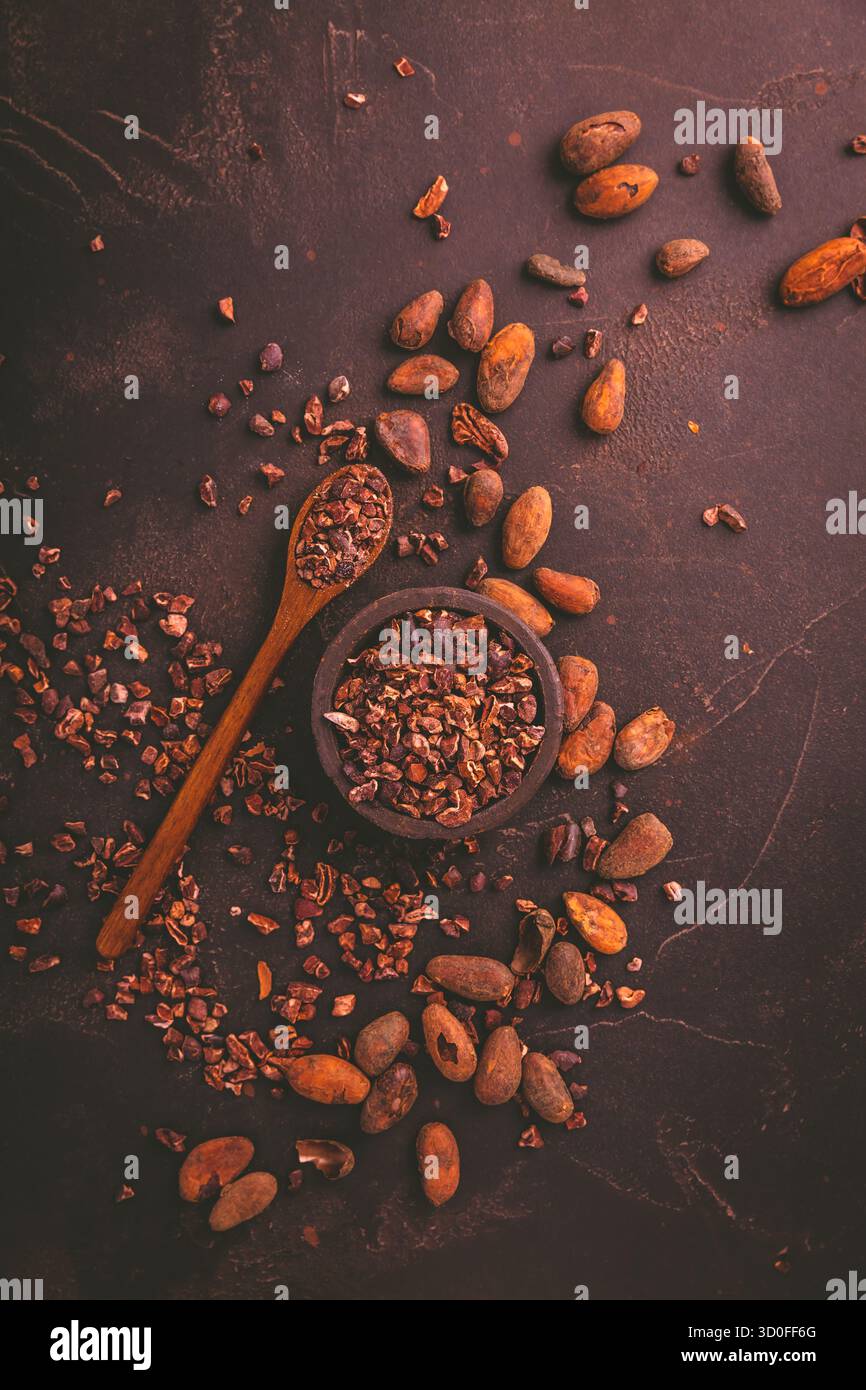 Pennini di cacao biologici e fagioli di cacao in un recipiente su sfondo marrone Foto Stock