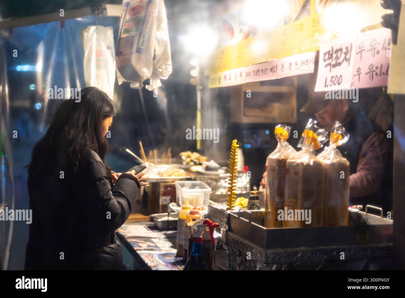 Donna che ordina cibo in uno stand di Street food di notte, con vapore che sale dall'area di cottura di Seoul, Corea del Sud, il 29 gennaio 2024 Foto Stock