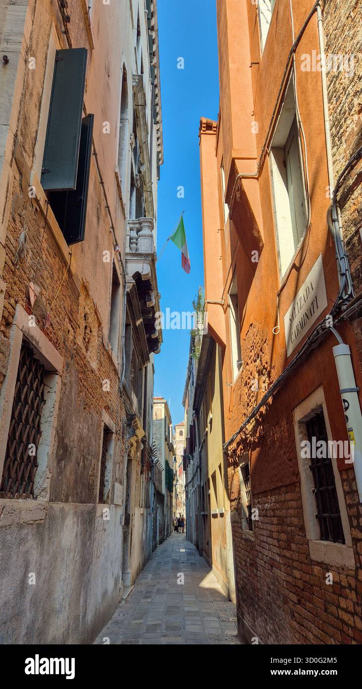 Vicolo stretto di Venezia, Italia, con bandiera italiana appesa, strada storica e architettura tradizionale. Foto Stock
