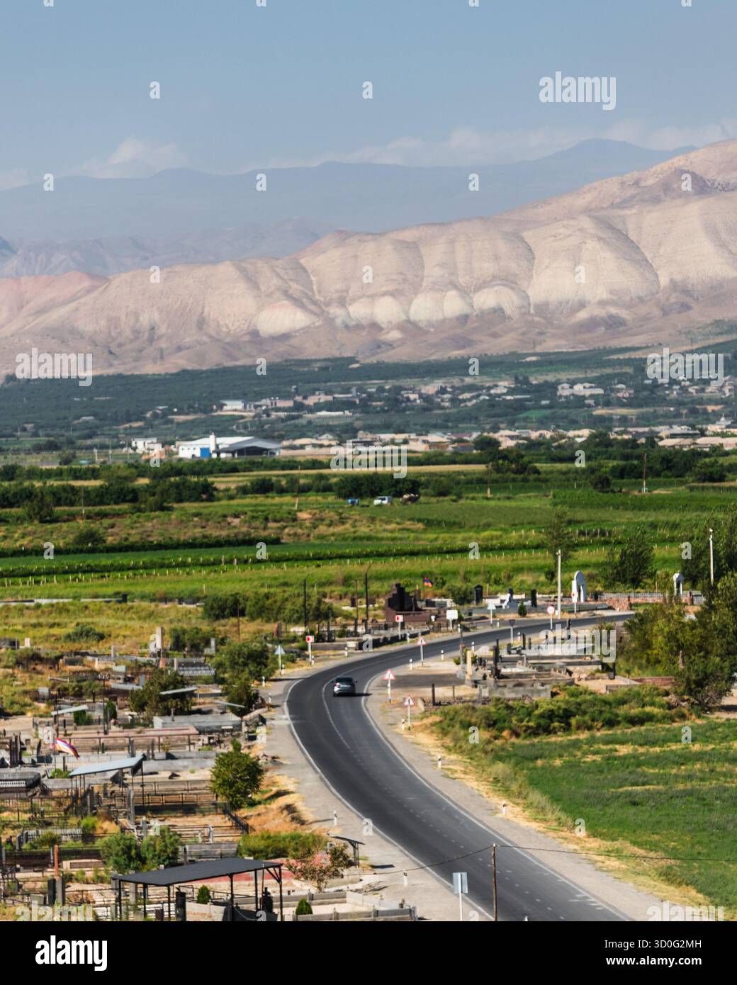 Veduta di una tortuosa strada asfaltata che attraversa un paesaggio verde vivace, incorniciata da montagne lontane sotto un cielo luminoso, Pokr veda, provincia di Ararat, Foto Stock