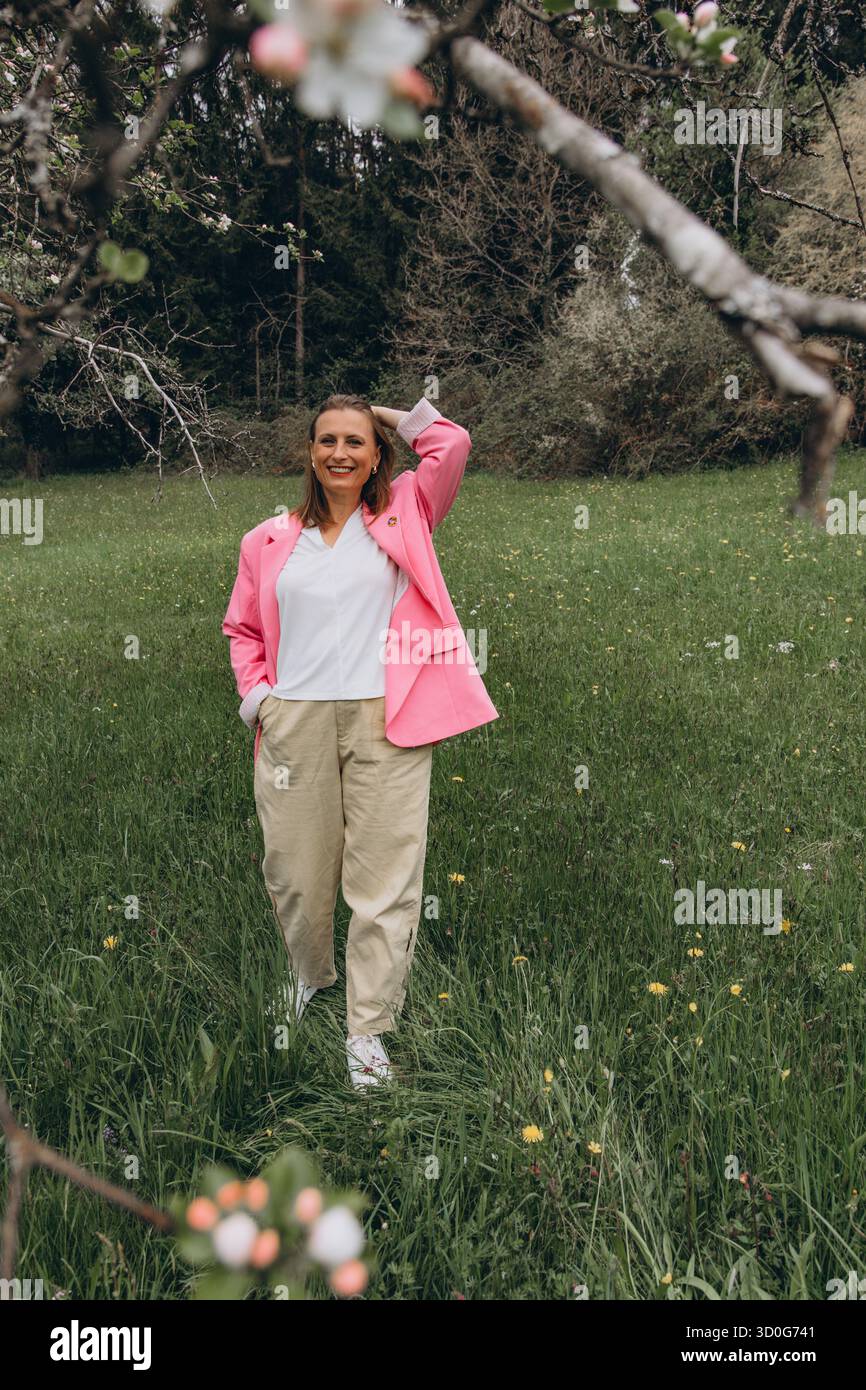 Donna di mezza età sicura in piedi in un giardino fiorito di primavera. Abbracciando la natura, l'autostima, la vitalità e la bellezza della femminilità matura in Fresh o Foto Stock