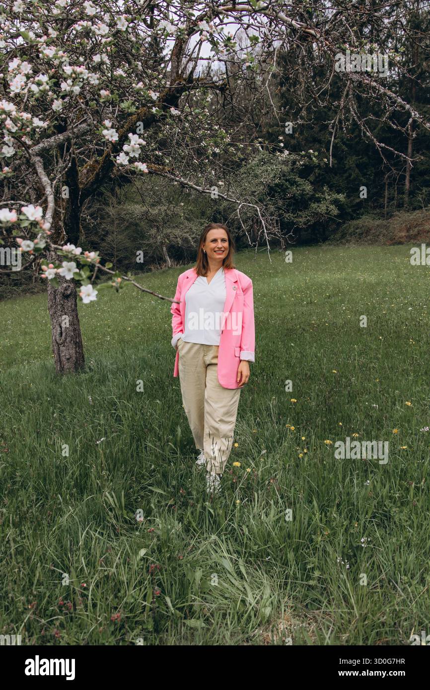Donna di mezza età sicura in piedi in un giardino fiorito di primavera. Abbracciando la natura, l'autostima, la vitalità e la bellezza della femminilità matura in Fresh o Foto Stock