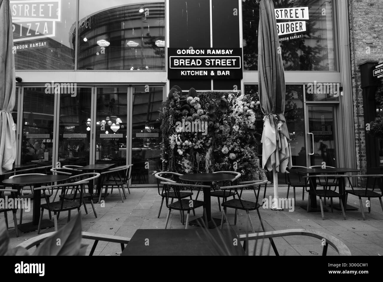 Foto in bianco e nero del Bread Street Kitchen & Bar di Gordon Ramsay a Liverpool, che mostra posti a sedere all'aperto e l'esterno del ristorante moderno. Foto Stock