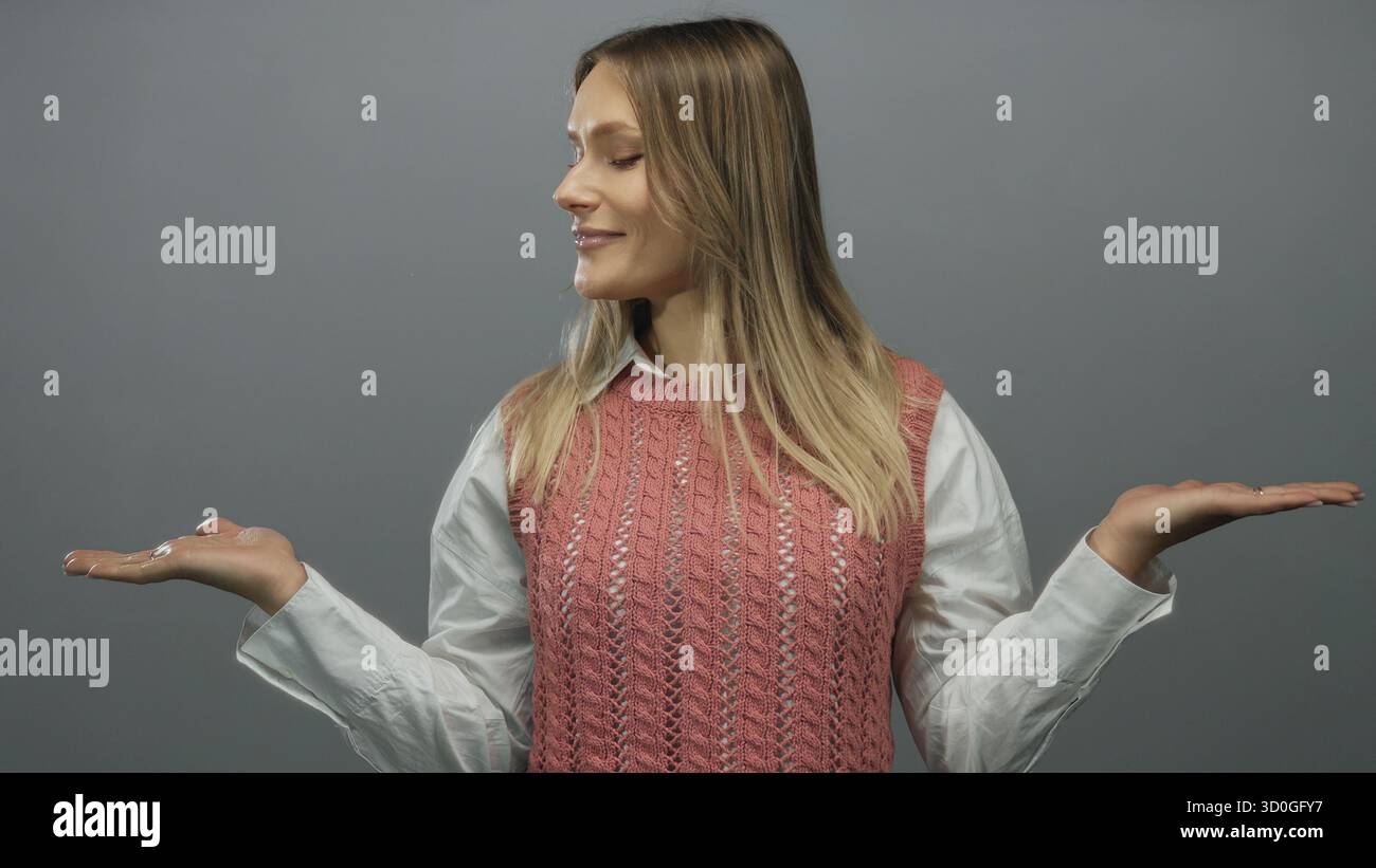Donna sorridente che regge su sfondo grigio isolato indossando gilet rosa e camicia bianca che trasuda felicità e positività Foto Stock