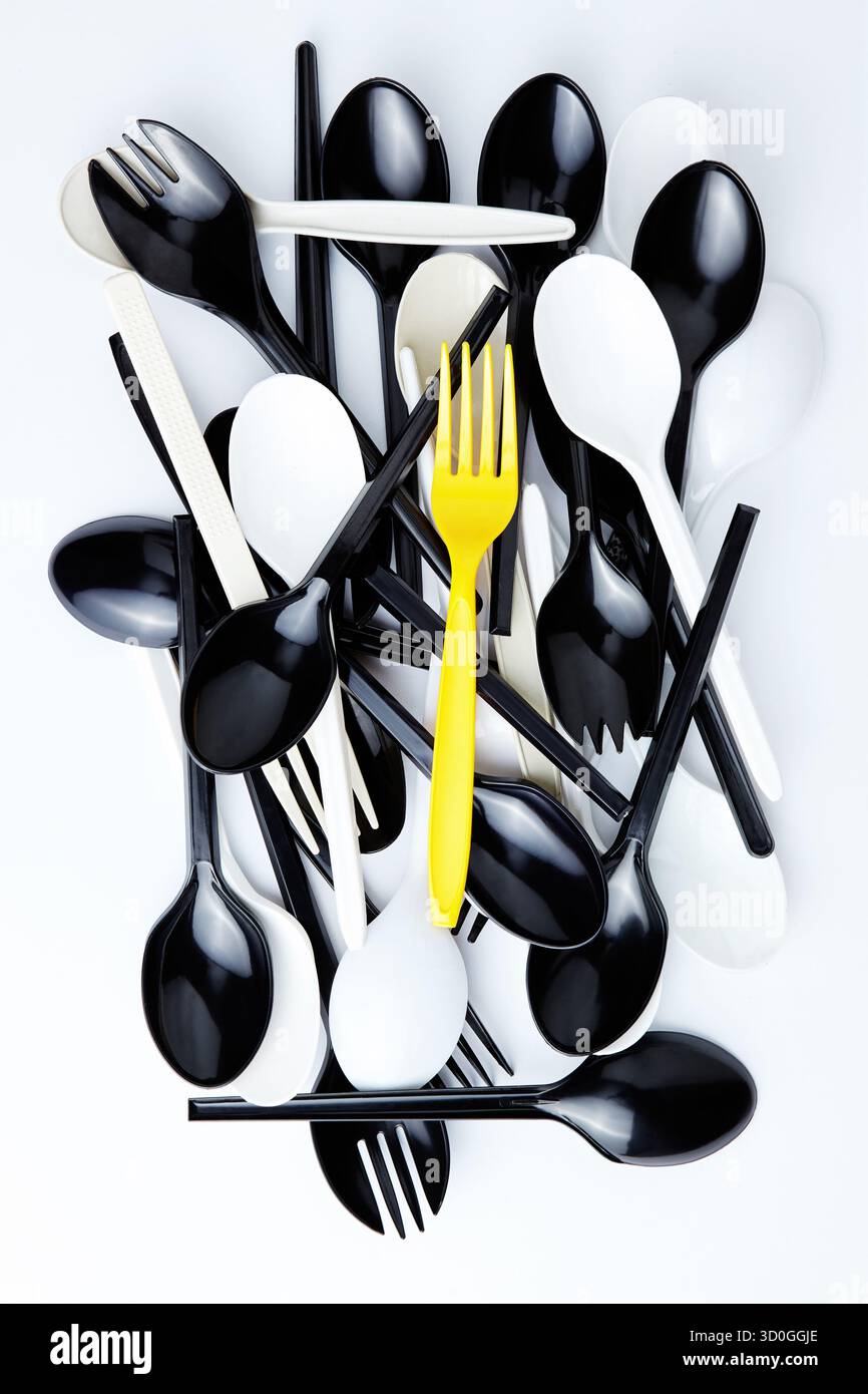 Una forchetta di plastica gialla sopra una pila di posate bianche e nere Foto Stock