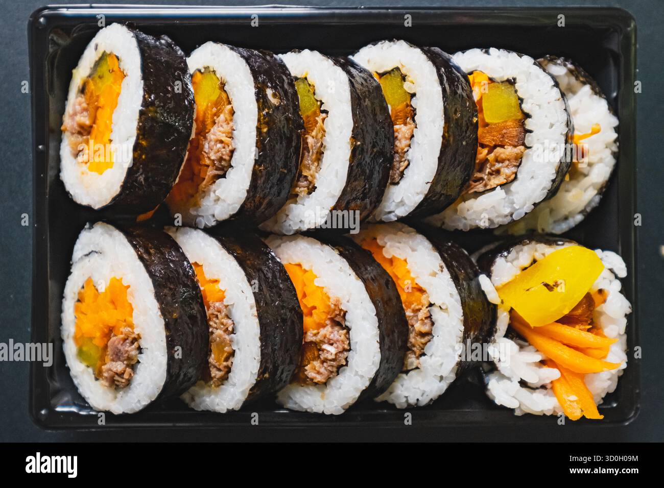 Un vassoio ordinato di involtini kimbap ripieni di riso, manzo, carote e ravanelli sottaceto, avvolti in alghe marine Foto Stock