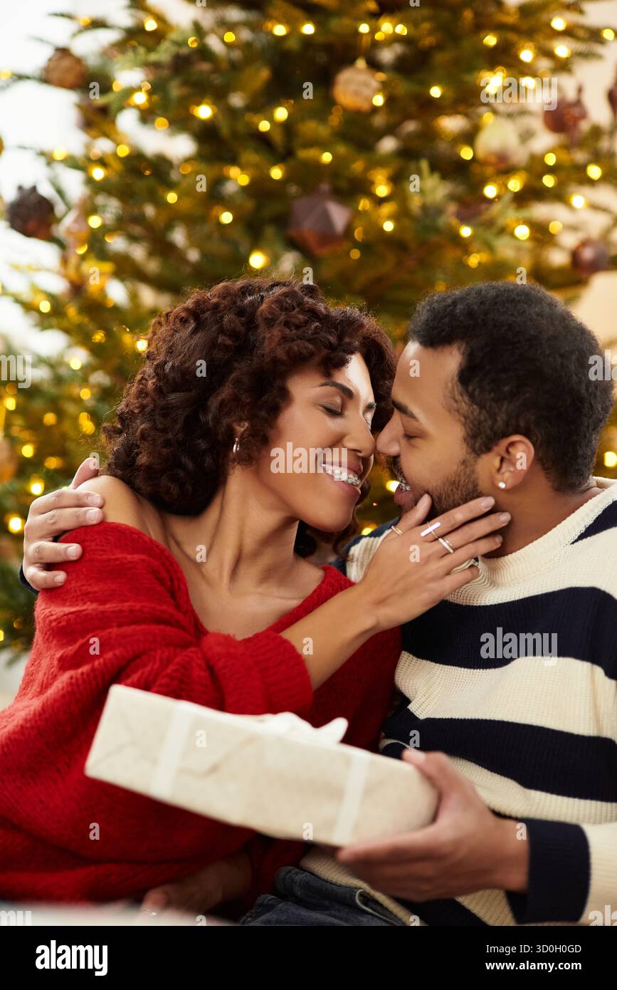 Una coppia felice condivide un momento tenero accanto all'albero di Natale splendidamente decorato, abbracciando l'amore. Foto Stock