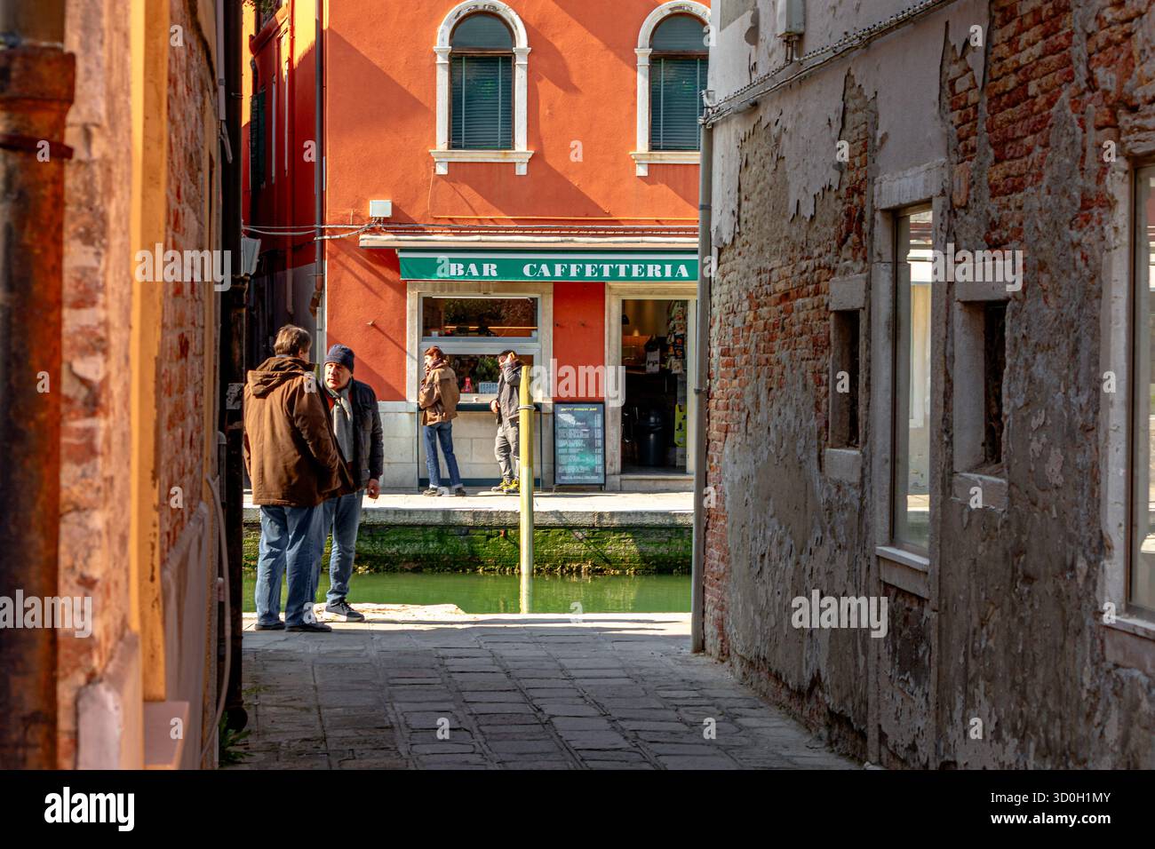 Due uomini che hanno una conversazione vicino ad uno stretto canale alla fine di un vicolo a Venezia, in Italia Foto Stock