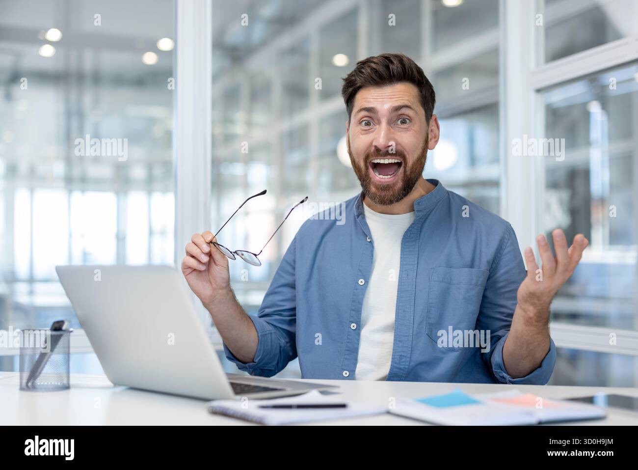 L'uomo d'affari del moderno computer portatile dell'ufficio reagisce con gioia e si alza la mano in festeggiamenti dopo aver letto buone notizie su promozioni, offerte o investimenti di successo Foto Stock