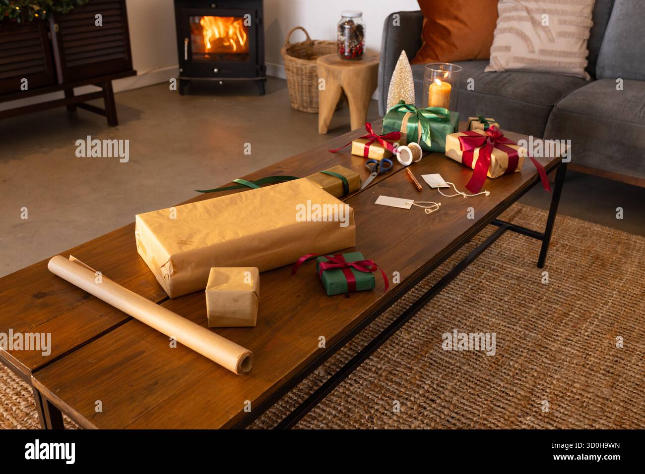 I regali avvolti e le etichette regalo si trovano sul tavolino da caffè in legno vicino alla stufa a legna Foto Stock
