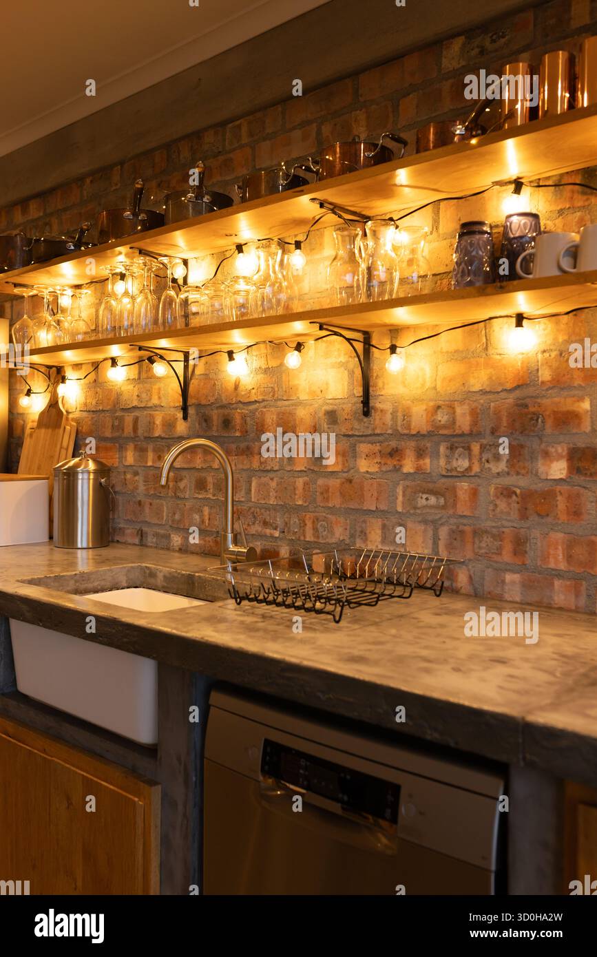 Il ripiano in pietra e i ripiani in legno incorniciano la cucina rustica con lavandino a incasso e luci a globo Foto Stock