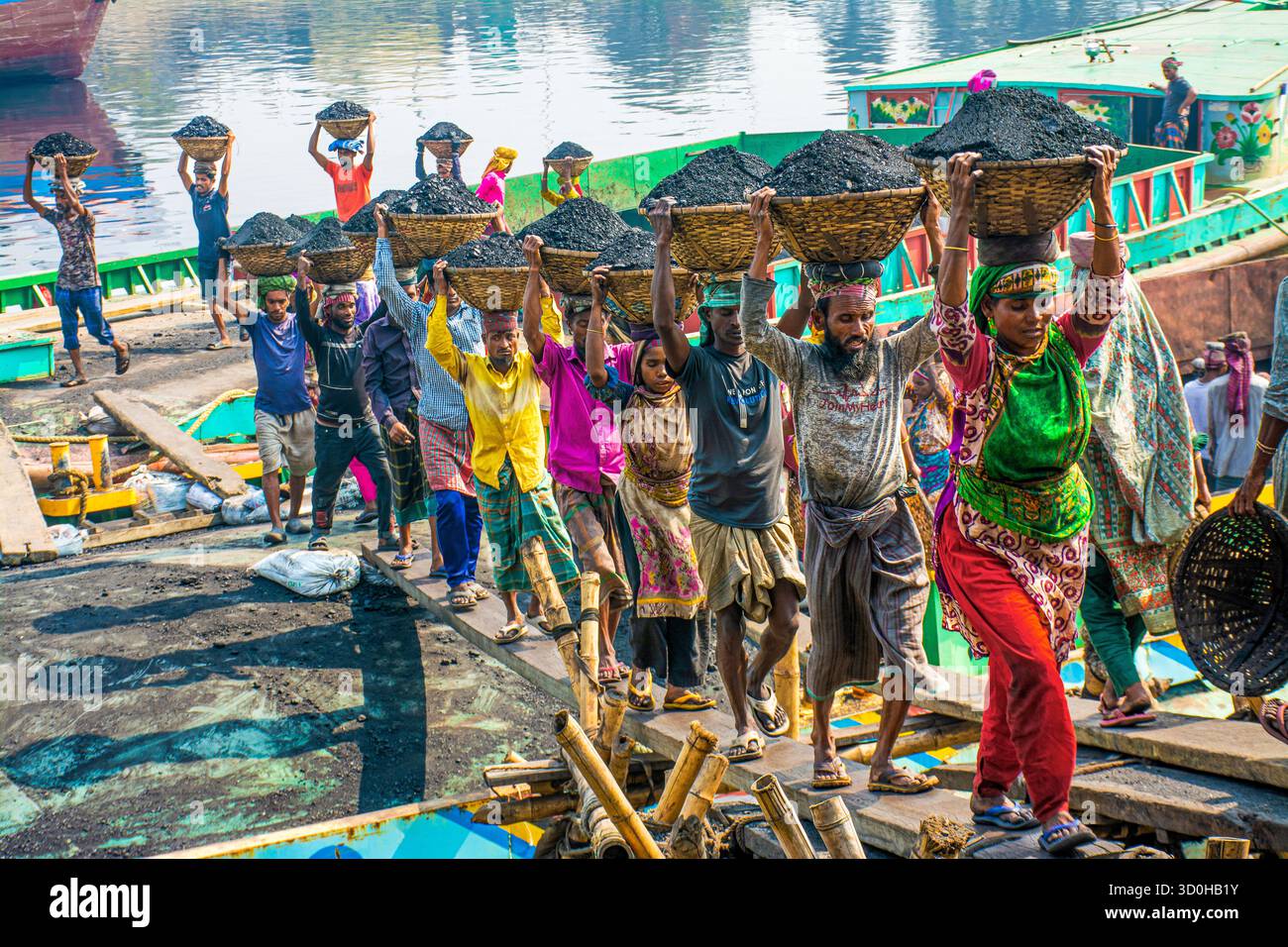 Dacca, Bangladesh - 15 aprile 2024: Vista dei lavoratori che trasportano cesti pieni di carbone sulla testa, una linea di colori vivaci sullo sfondo del Foto Stock