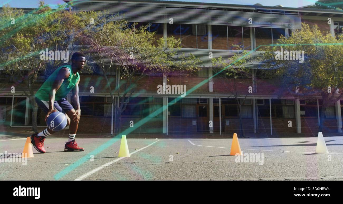 Atleta che indossa una maglia verde che dribbla pallacanestro blu attraverso i coni sul campo scolastico, copia spazio Foto Stock