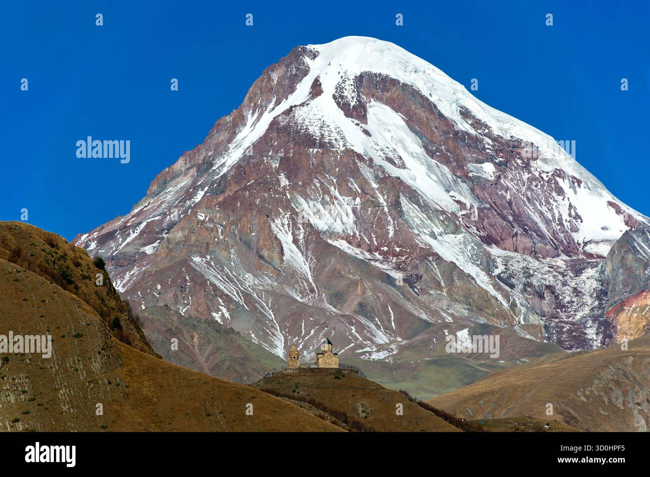 La cima innevata e ghiacciata del monte Kazbek, a sinistra sotto la chiesa della Trinità di Gergeti, Stepantsminda, Georgia Foto Stock