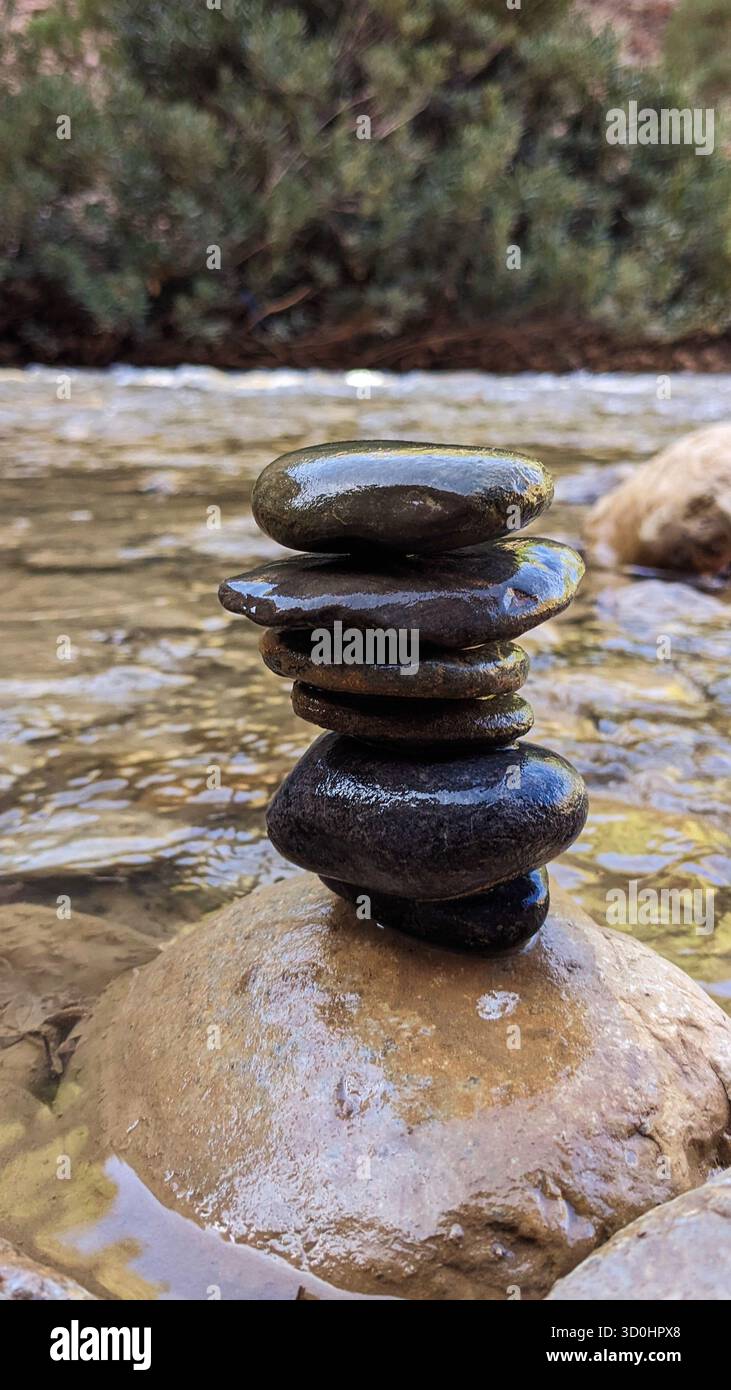 pile di pietre lisce e bagnate bilanciate su una roccia in un fiume che scorre - simboleggiano equilibrio, consapevolezza e armonia con la natura Foto Stock