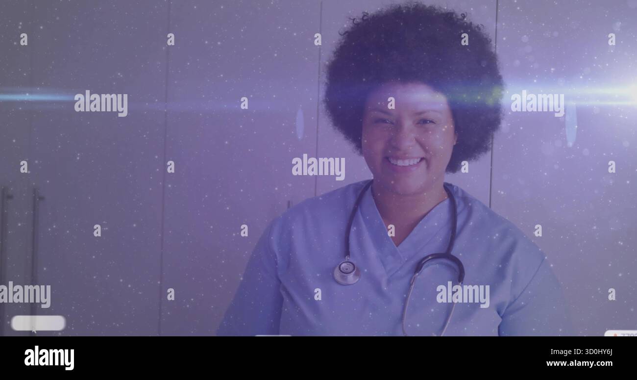 Infermiera sorridente che indossa scrub blu e stetoscopio in piedi nella sala esame con armadi di stoccaggio bianchi Foto Stock