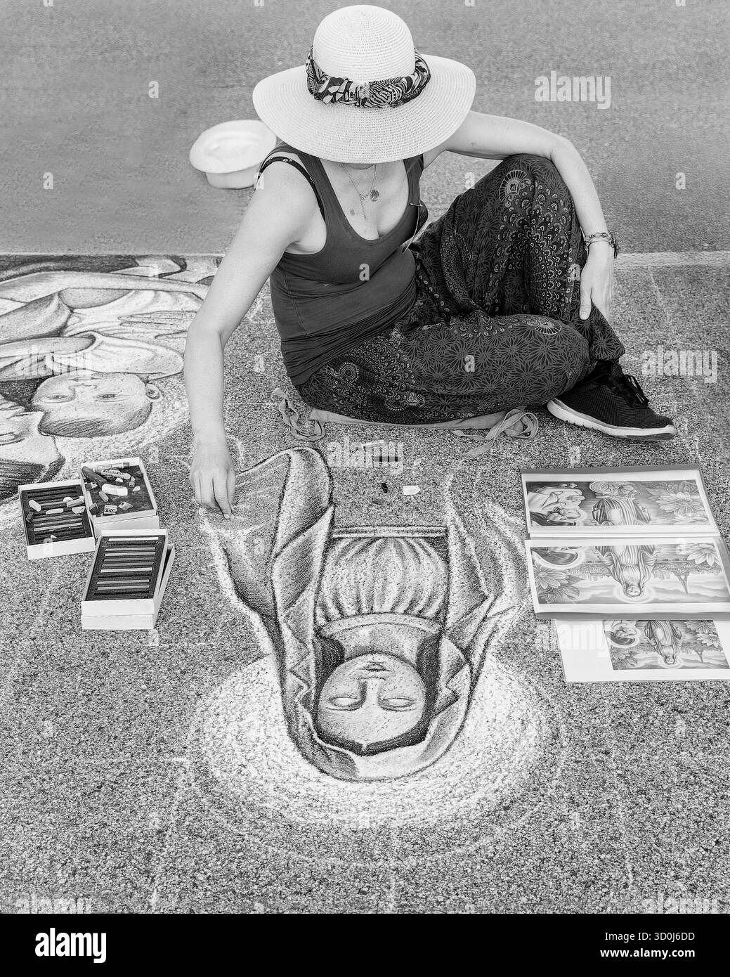 Artista di strada che crea un disegno in gesso di una figura religiosa sul marciapiede durante un evento artistico all'aperto. Immagine in bianco e nero. Foto Stock