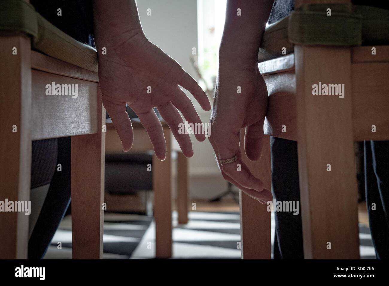Due persone sedute fianco a fianco che si avvicinano per le mani sotto le sedie in casa Foto Stock