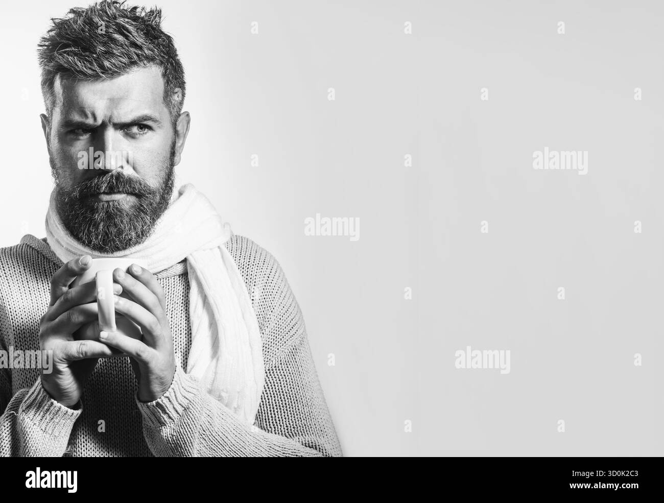 L'ora del caffè. Uomo barbuto serio in maglia e sciarpa bevendo una tazza di tè o caffè. Bell'uomo in abiti caldi informali con tazza di move calda Foto Stock