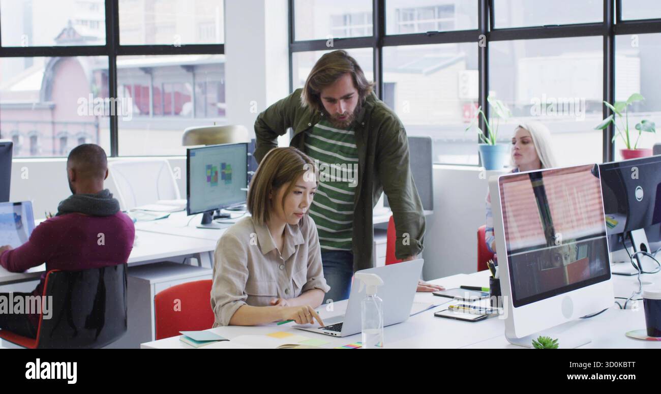 Collaborare con i colleghi che si appoggiano su un notebook in un ufficio open space, con monitor e impianti in vaso Foto Stock